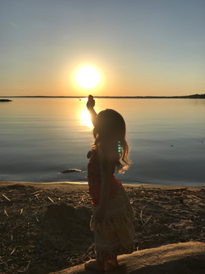 Child on lakeshore posing with sunset.